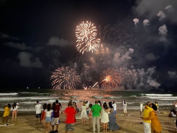Espectáculo de fuegos artificiales en la playa, disfrutando con amigos y familiares.
